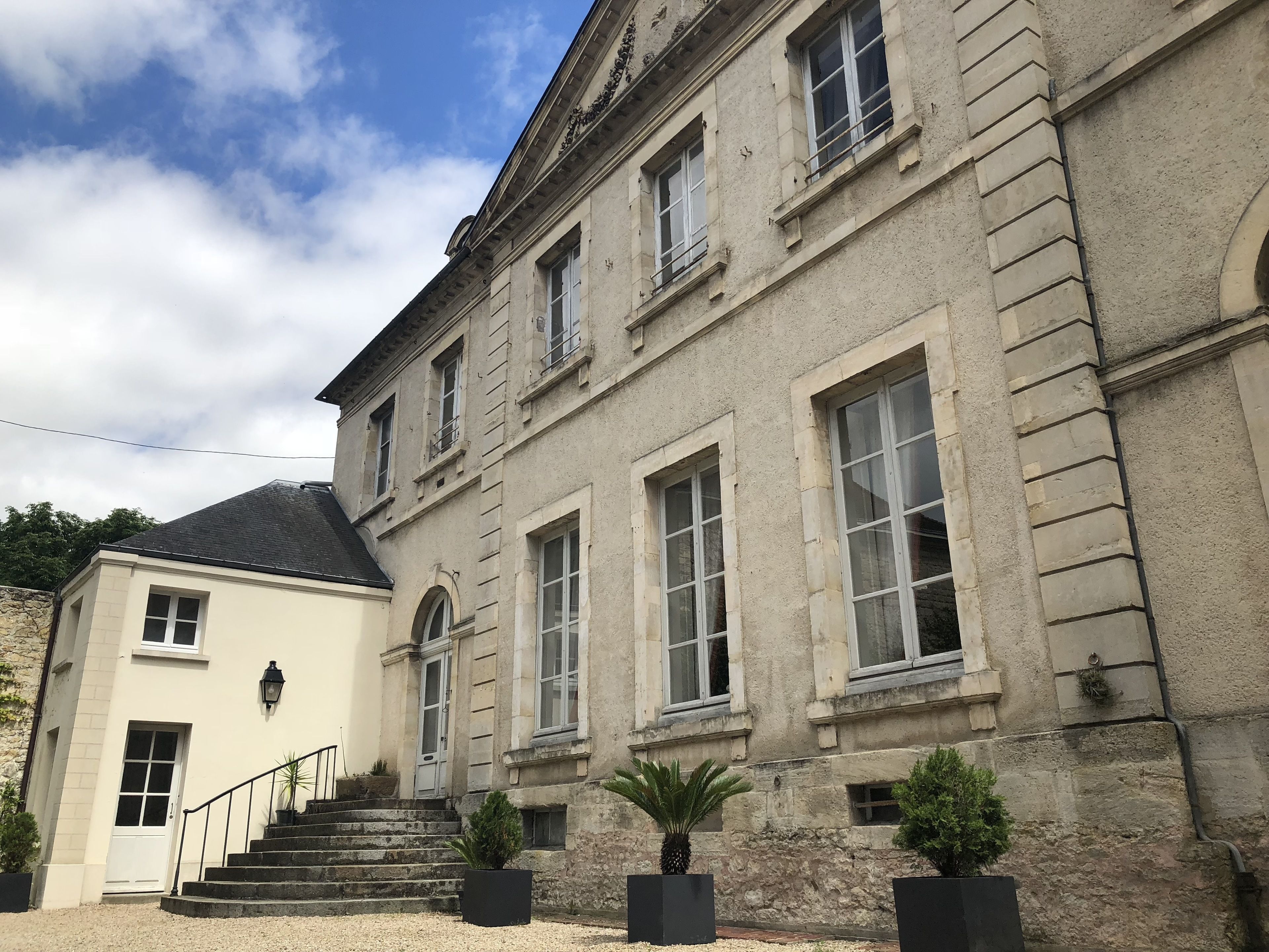 Un bâtiment à deux étages, doté d’une façade en pierre, de grandes fenêtres et d’un escalier menant à l’entrée.