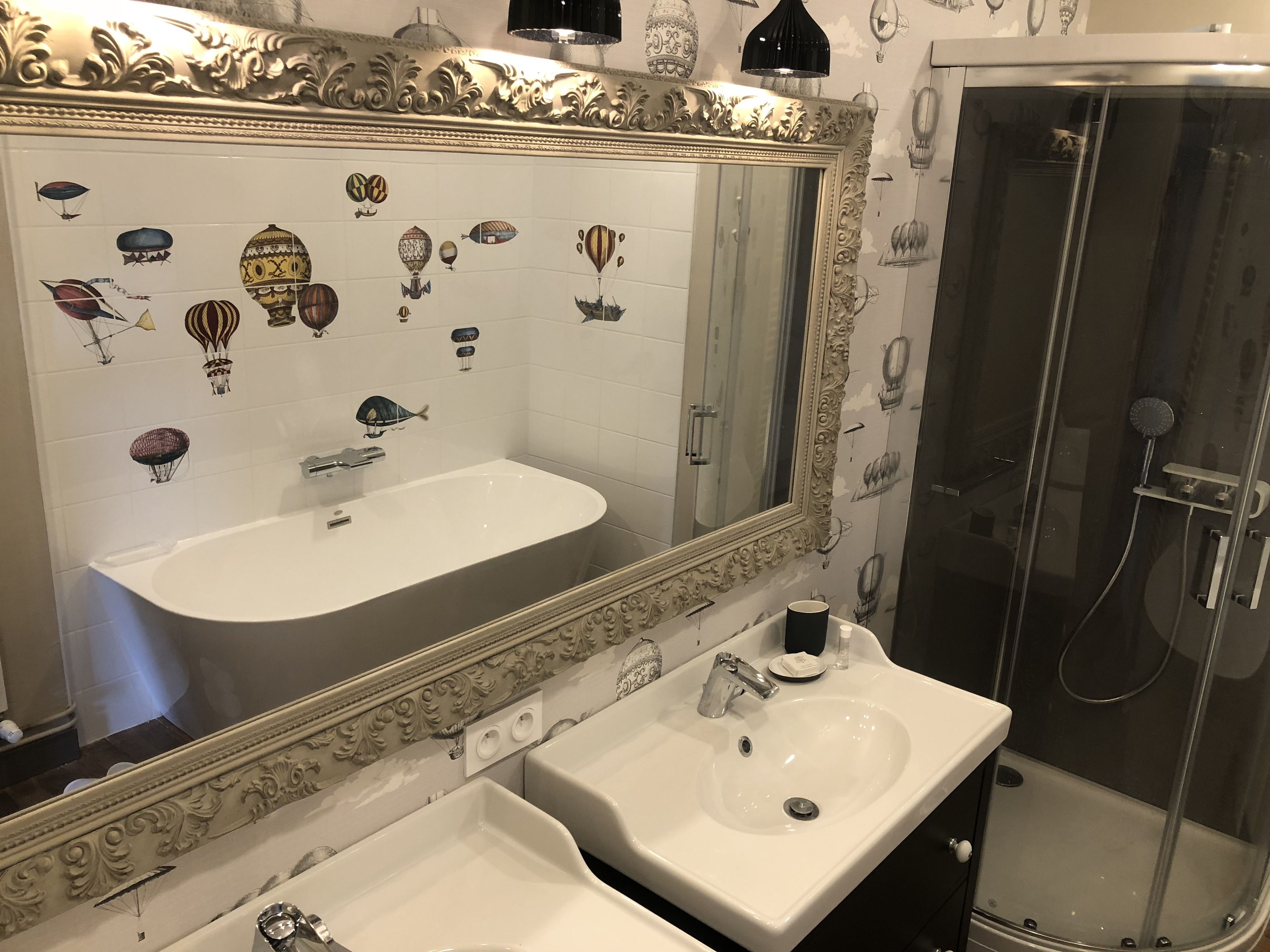 Une salle de bain avec un grand miroir, deux lavabos et une douche.