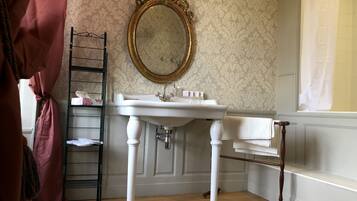 Un baño con un lavamanos blanco pedestal, un espejo con marco dorado, suelo de madera y pared con diseño.