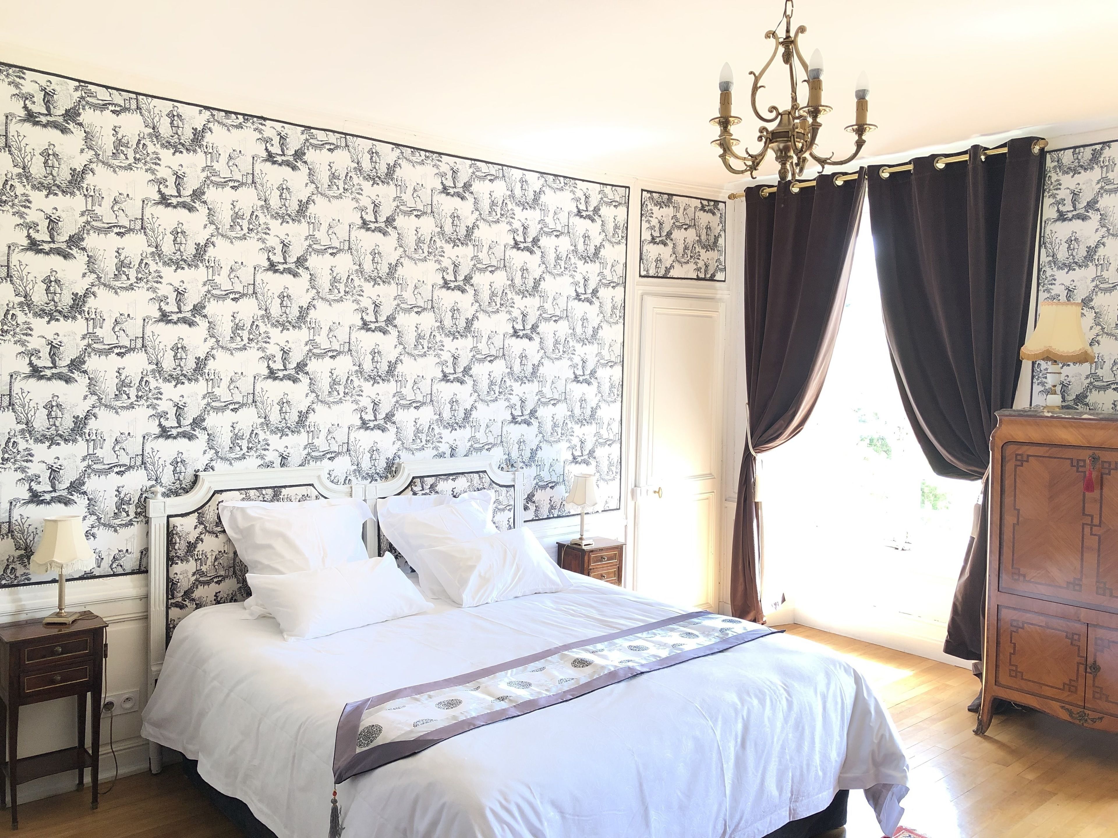 A bedroom with a bed, a nightstand, a dresser, and a window with curtains.