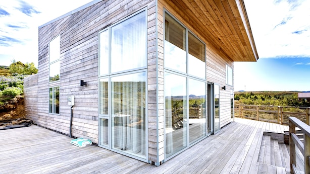 Una casa moderna con terraza de madera, grandes ventanales y techo de madera.
