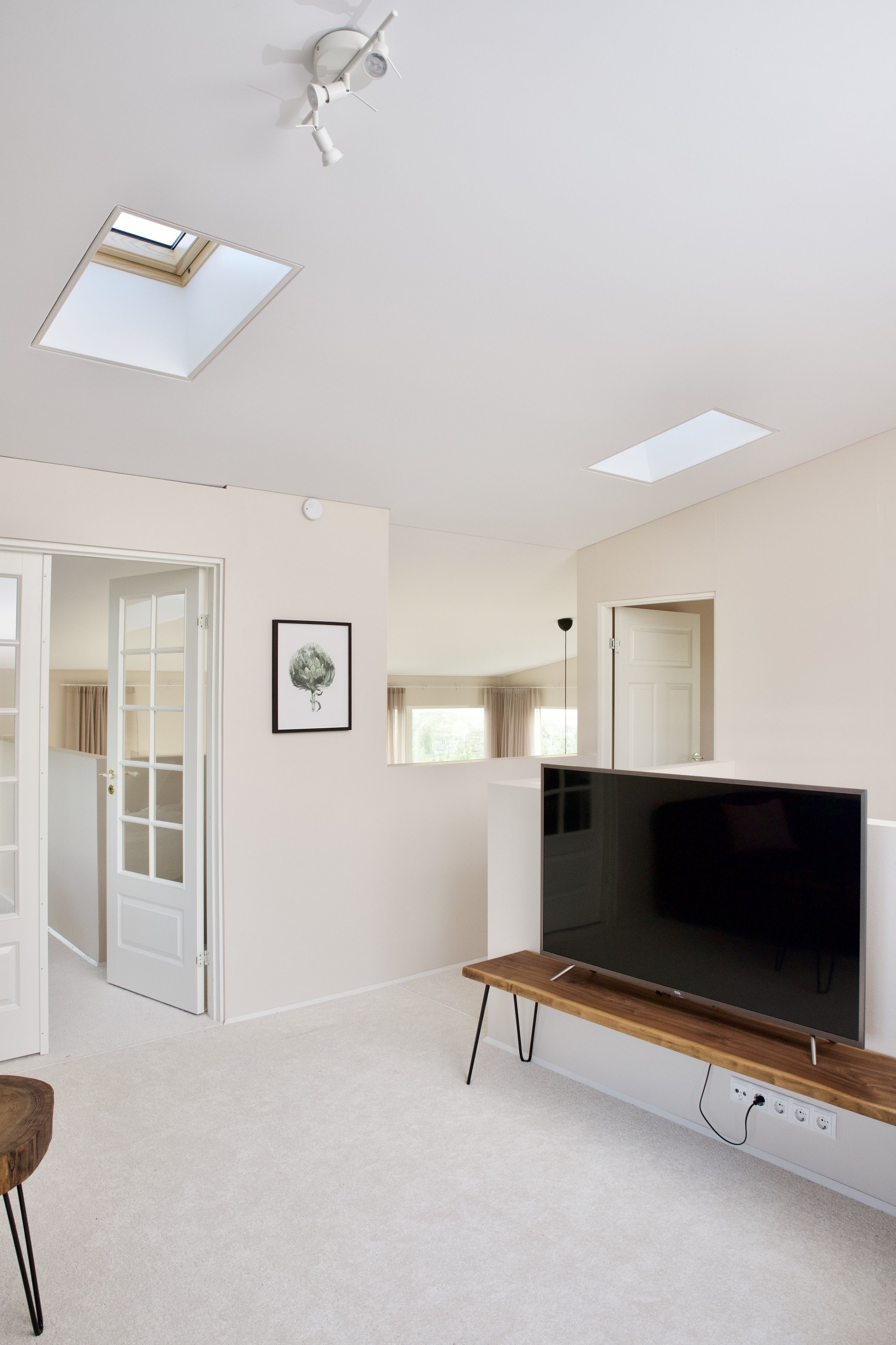 Un salon moderne avec un téléviseur à écran plat posé sur un meuble en bois, un ventilateur de plafond et une lucarne.