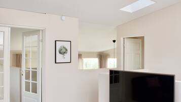A modern living room with a flat-screen TV on a wooden stand, a ceiling fan, and a skylight.