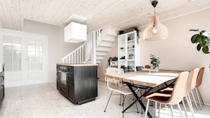 Cocina moderna con escalera de madera, armarios blancos y un comedor con mesa y sillas de madera.