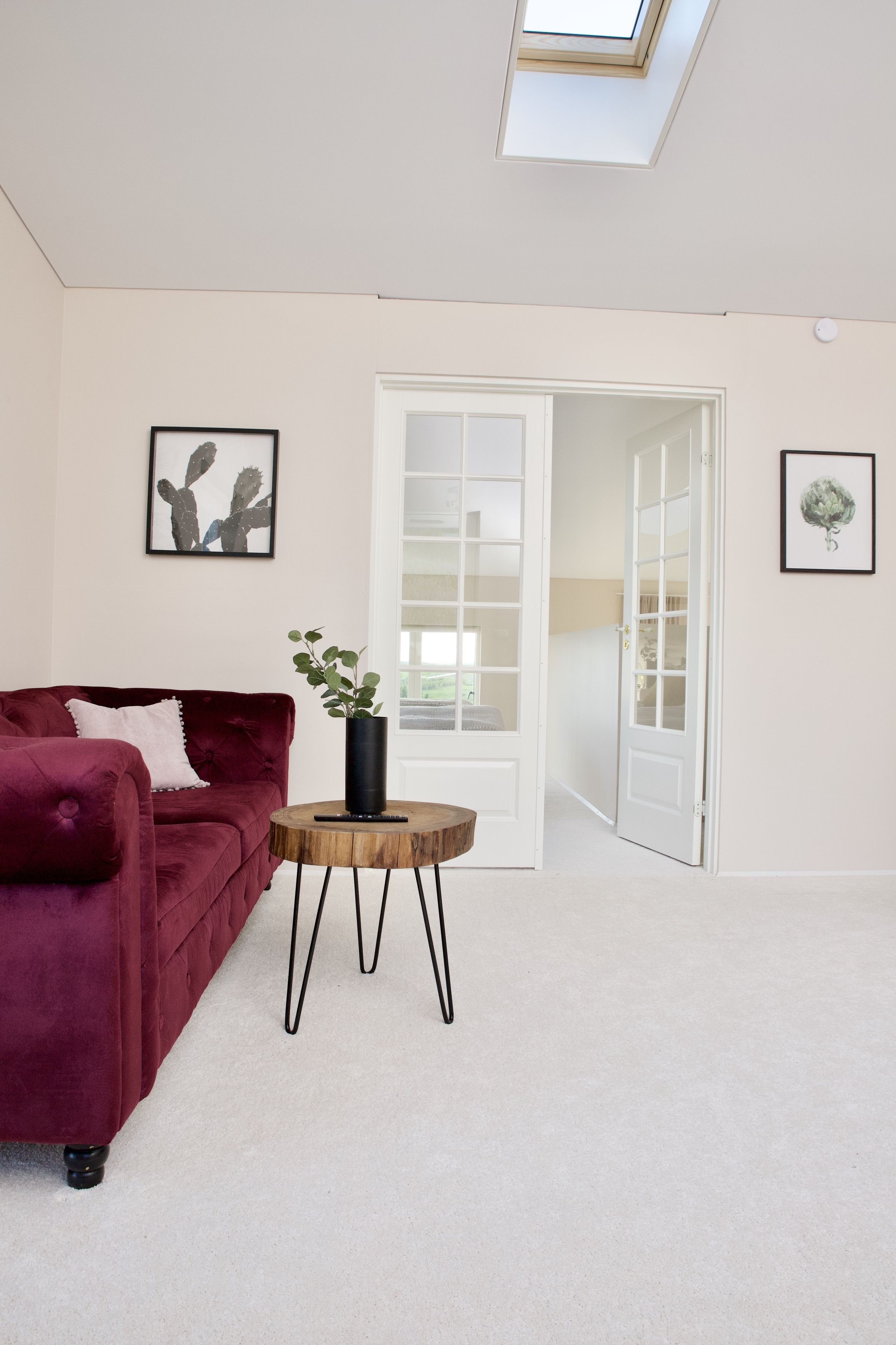 A room with a red velvet sofa, a small wooden side table with a plant, and a white door leading to another room.