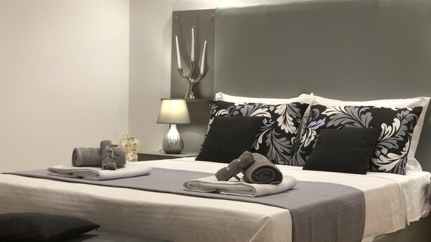 A modern bedroom with a large bed, a bedside table with a lamp, and decorative pillows.
