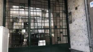A green metal gate with intricate patterns, a tiled wall, and a small trash bin.