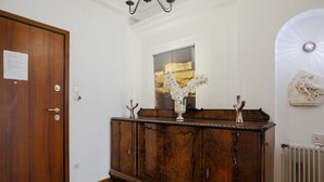 A hallway with a wooden door, a radiator, and a decorative cabinet with a framed picture above it.
