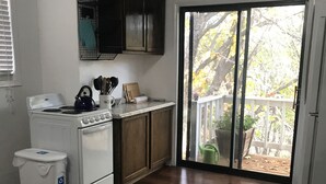 Une cuisine équipée d’une cuisinière, de placards et offrant une vue sur l’extérieur grâce à une porte-fenêtre coulissante.