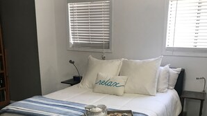 Un lit bien fait, recouvert d’une couverture à rayures, une table de chevet avec une lampe et une fenêtre avec des stores.