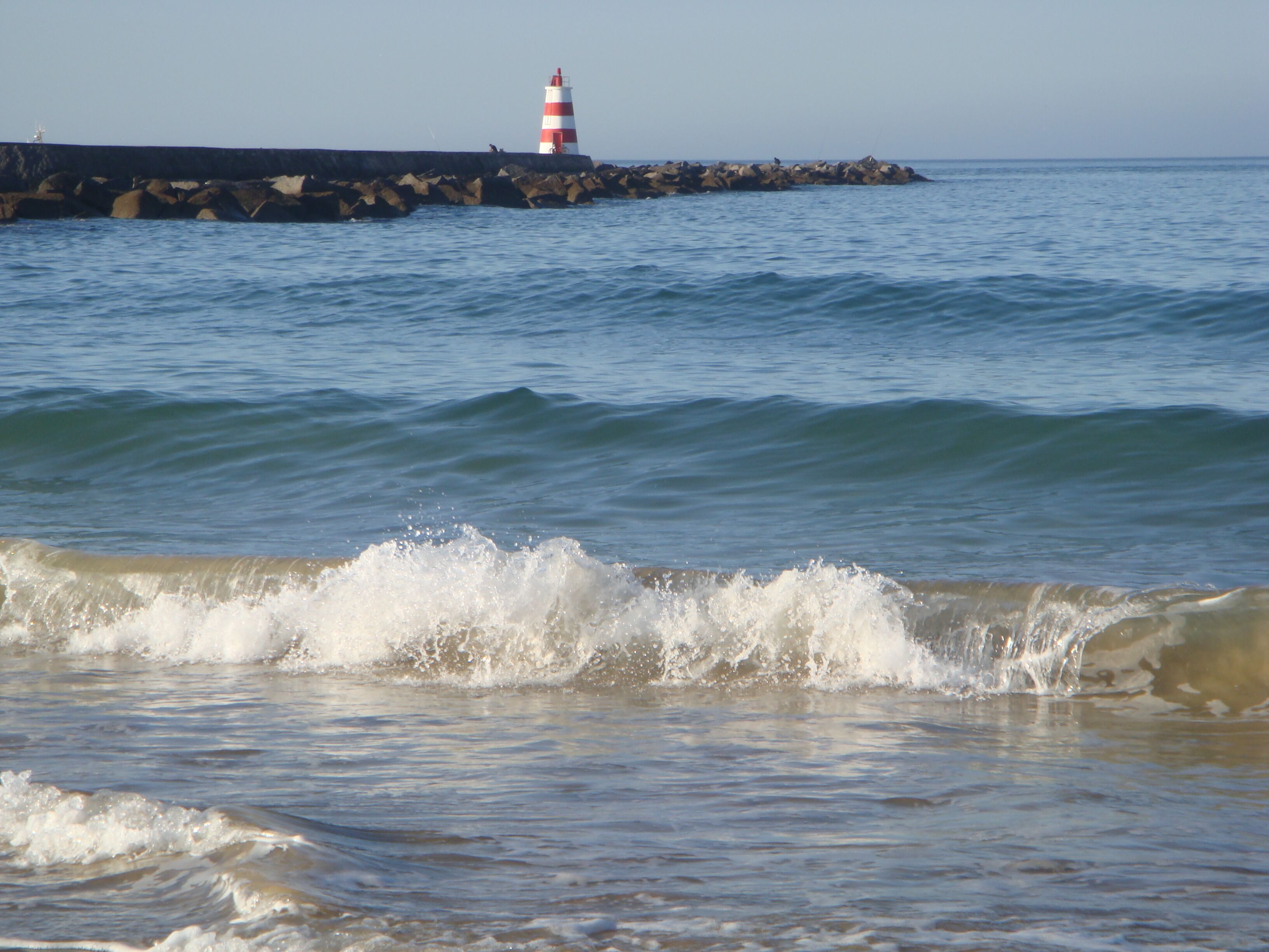 A lighthouse on a rocky pier with waves crashing onto the shore.