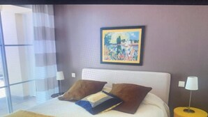 Ein Hotelzimmer mit einem großen Bett, zwei Kissen, einem gerahmten Gemälde an der Wand und zwei Nachttischen mit Lampen.