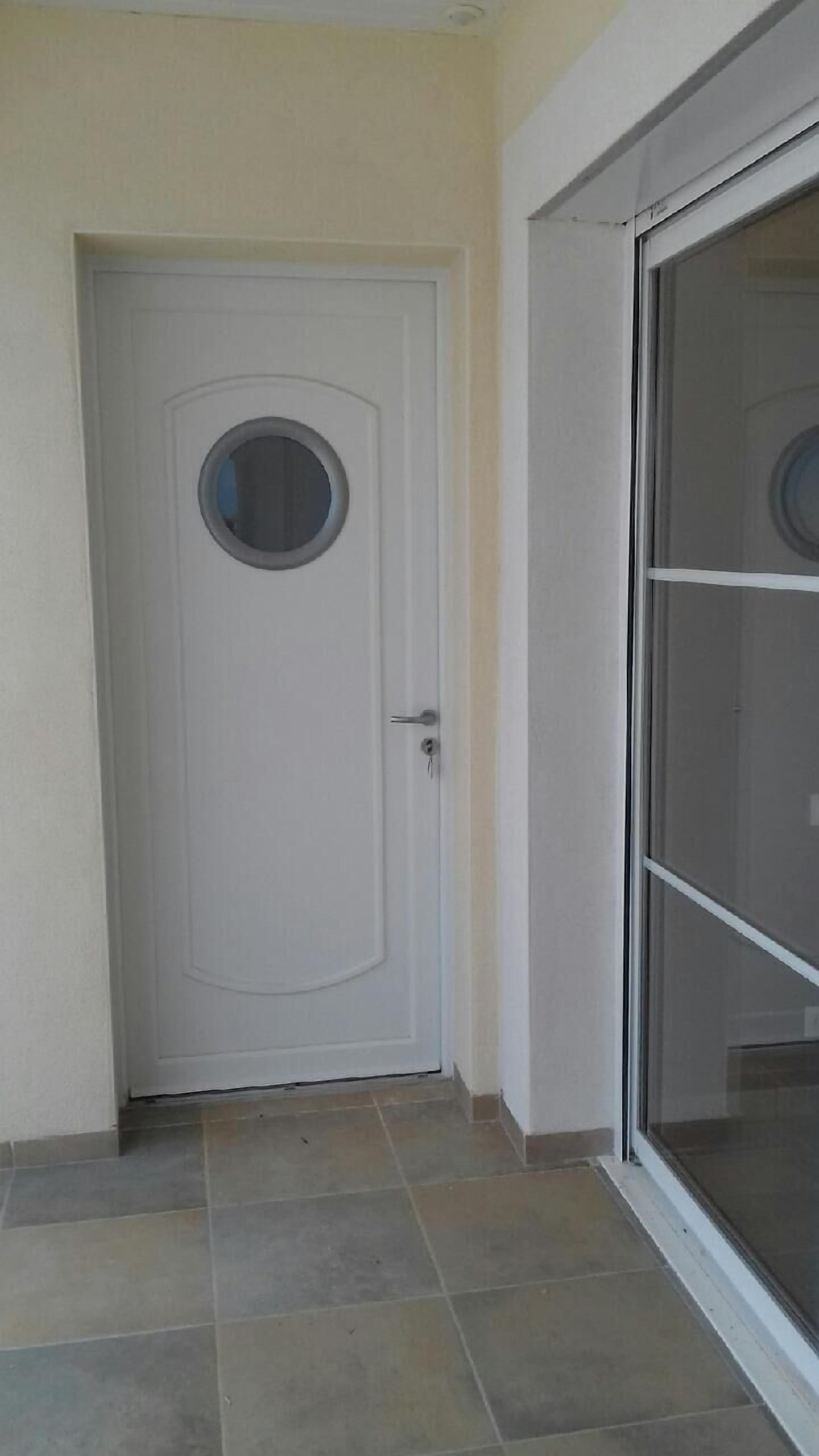 Une porte blanche avec une fenêtre ronde et une porte vitrée coulissante sur le côté droit.