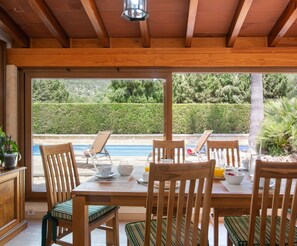 Un espace repas avec vue sur une piscine, des meubles en bois et une pergola agrémentée d’une lanterne.