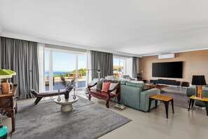 A spacious living room with a large flat-screen TV, comfortable seating, and a view of the ocean. - Oceanfront Villa at Praia Grande · Heated Pool (Colares)