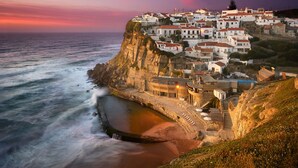 A coastal town with buildings on a cliff overlooking the sea, featuring a paved walkway along the coastline. - Oceanfront Villa at Praia Grande · Heated Pool (Colares)