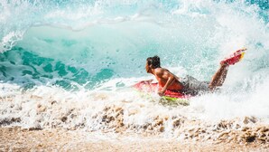 A person surfing on a wave with a red surfboard. - Oceanfront Villa at Praia Grande · Heated Pool (Colares)