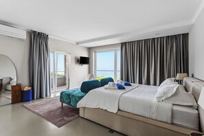 Ein modernes Schlafzimmer mit einem großen Bett, einem an der Wand montierten Fernseher und einem Balkon mit Vorhängen.