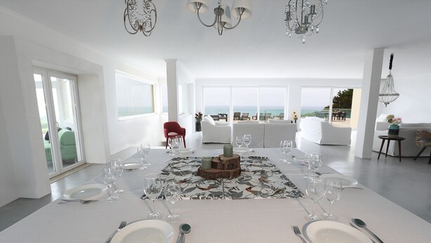 A dining area with a table set for four, large windows, and a view of the sea. - Oceanfront Villa at Praia Grande · Heated Pool (Colares)