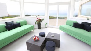 A bright room with two green sofas, a wicker coffee table, and a view of the sea.