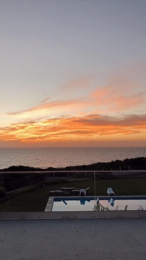 Vista al atardecer desde un balcón con piscina y sillones de descanso.