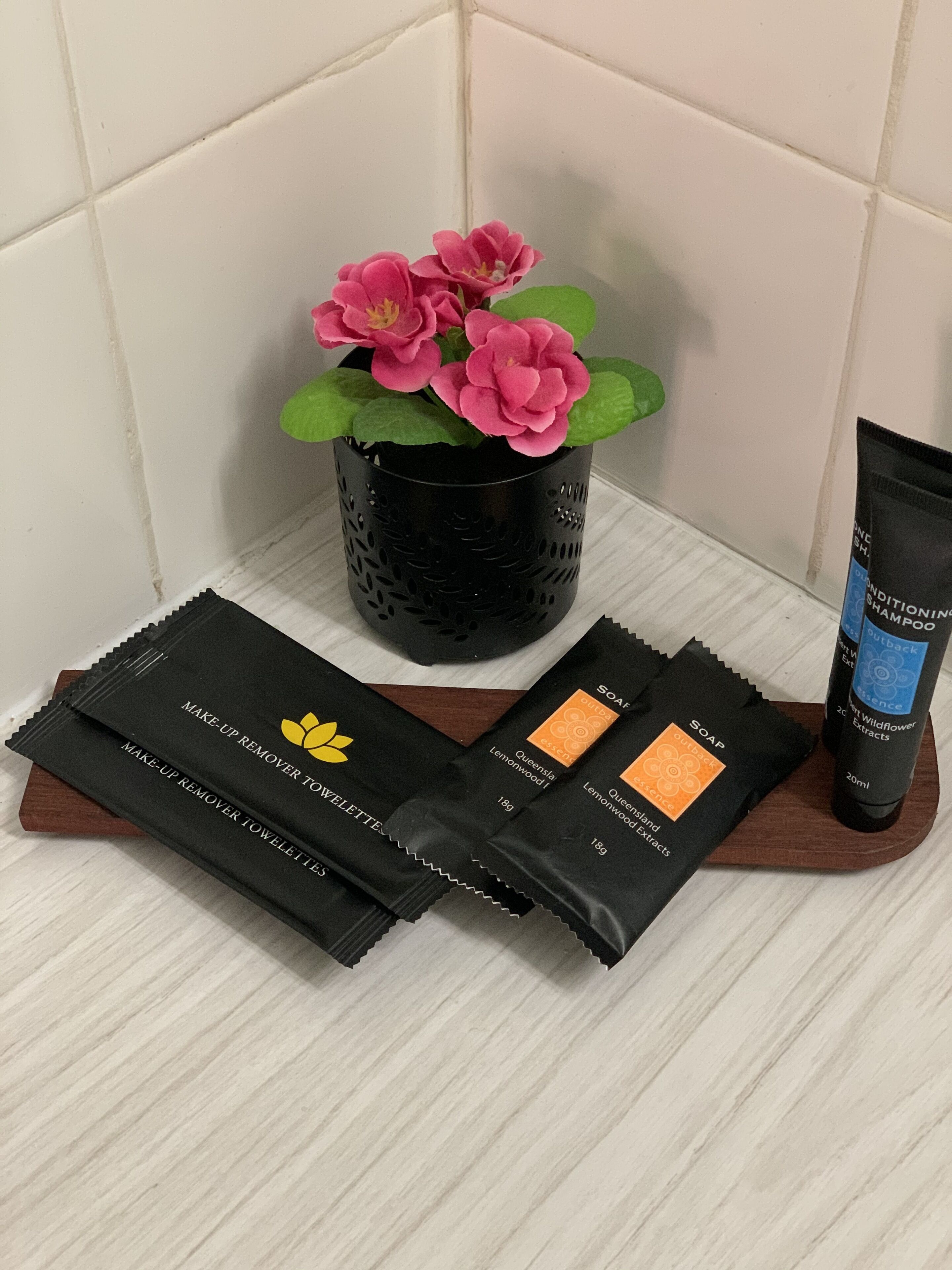 A bathroom vanity with a black soap dispenser, a tube of shampoo, and two makeup remover towelettes.