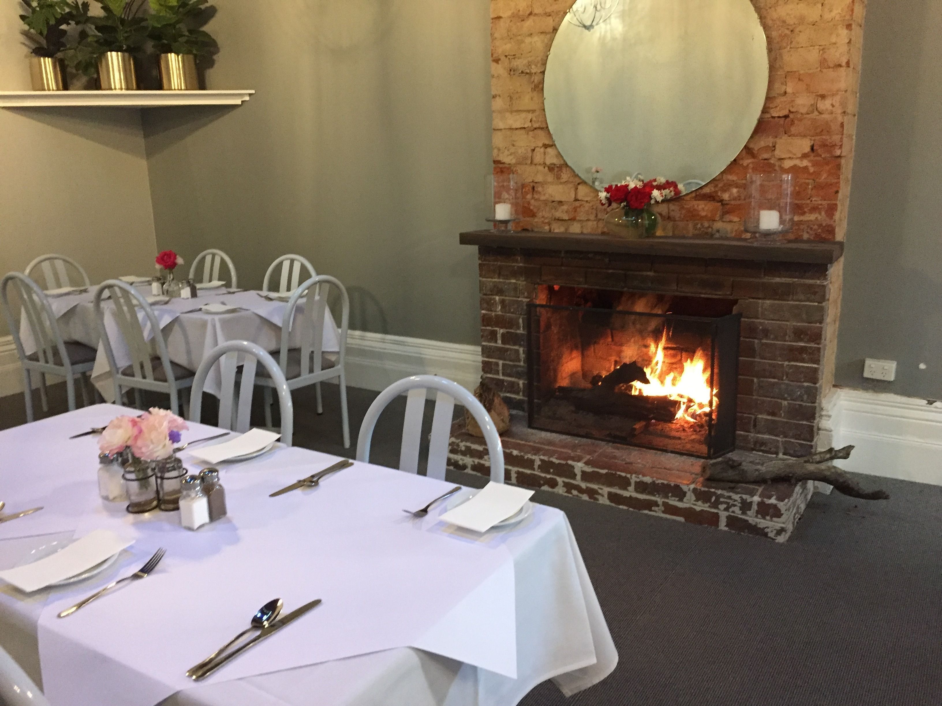 Comedor con chimenea de ladrillo, sillas blancas y una mesa dispuesta para cuatro.