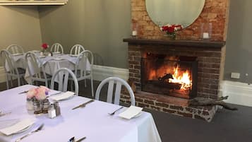 Comedor con chimenea de ladrillo, sillas blancas y una mesa dispuesta para cuatro.