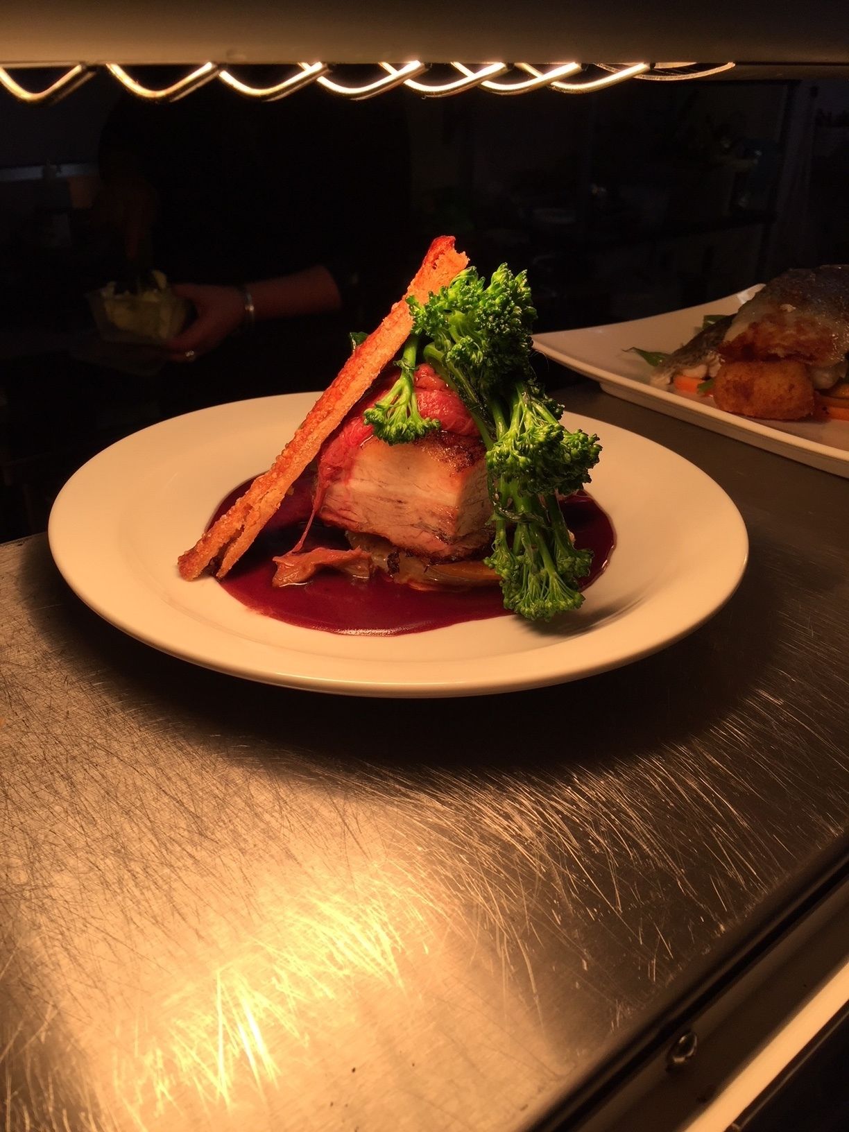 A plated dish with a piece of meat, broccoli, and a sauce on a white plate.