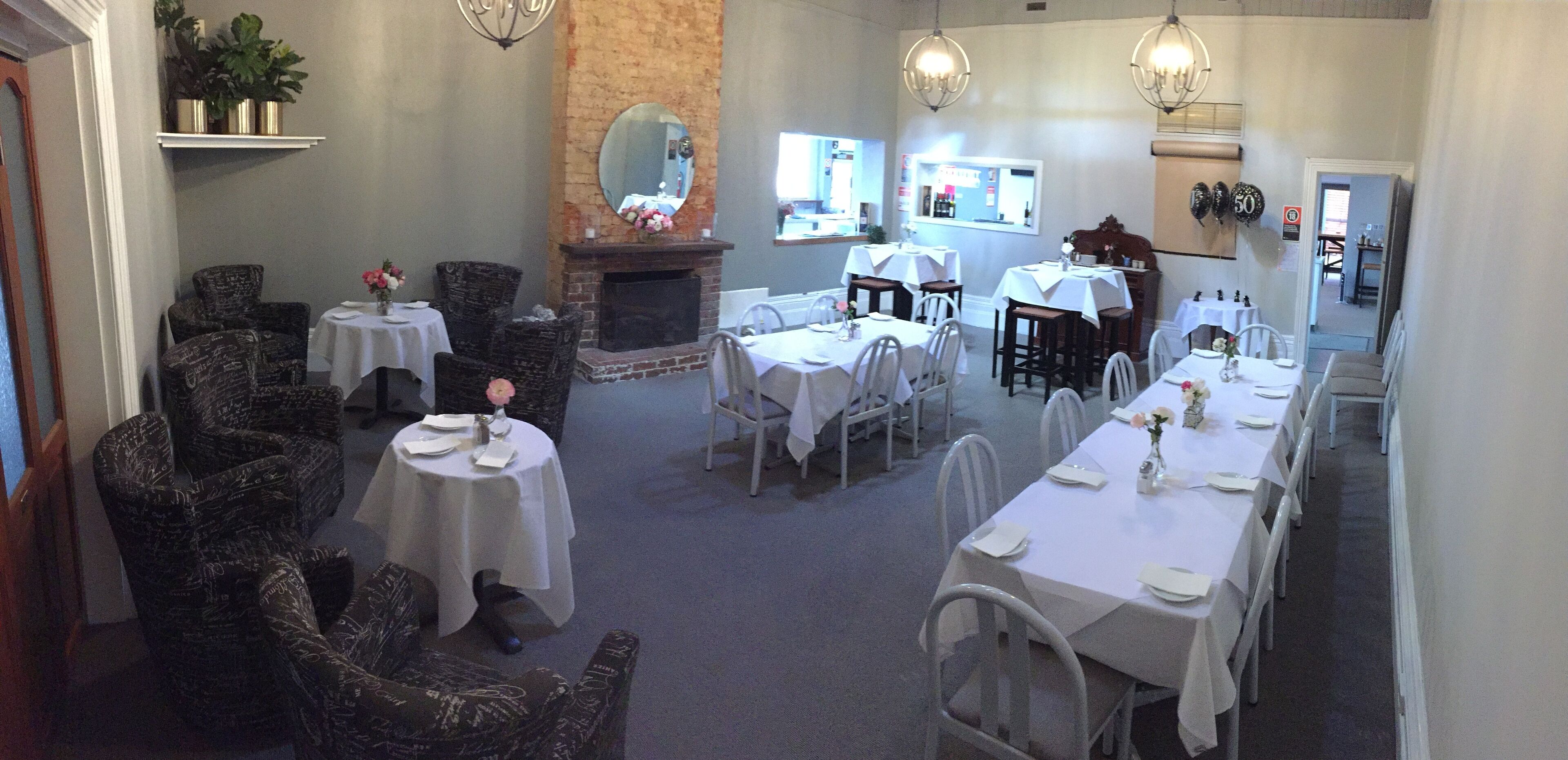 A restaurant with multiple tables and chairs, a brick fireplace, and hanging light fixtures.