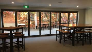 A spacious indoor area with large sliding glass doors leading to an outdoor patio. Inside, there are multiple wooden tables and benches arranged for dining or socializing.