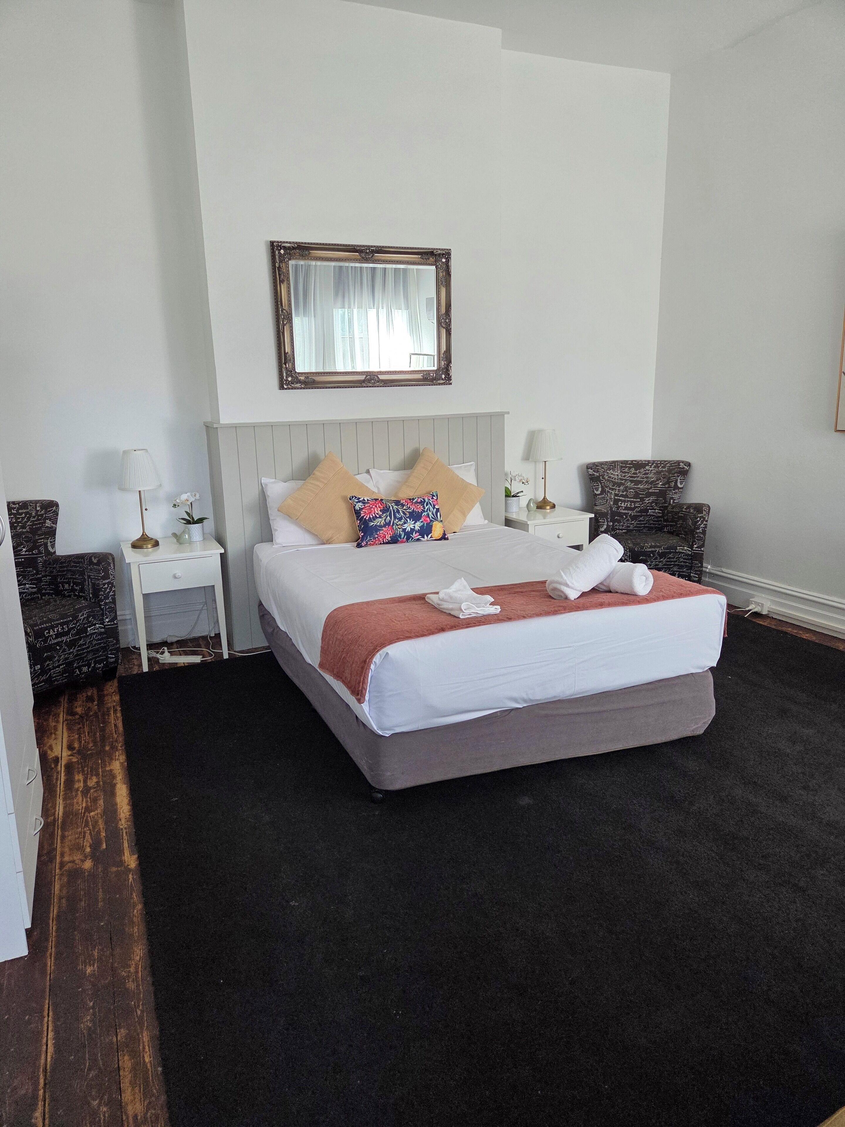 Een netjes ingerichte hotelkamer met een groot bed, twee nachtkastjes, een spiegel en een stoel.