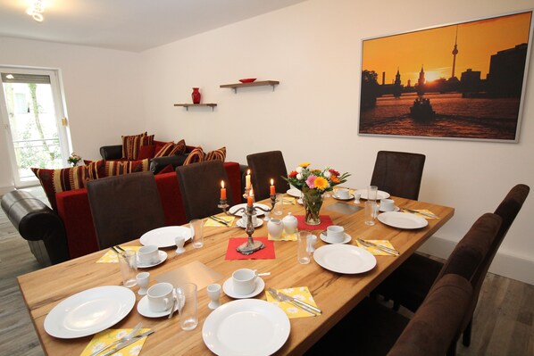A dining room with a wooden table set for a meal, chairs, and a sofa in the background.