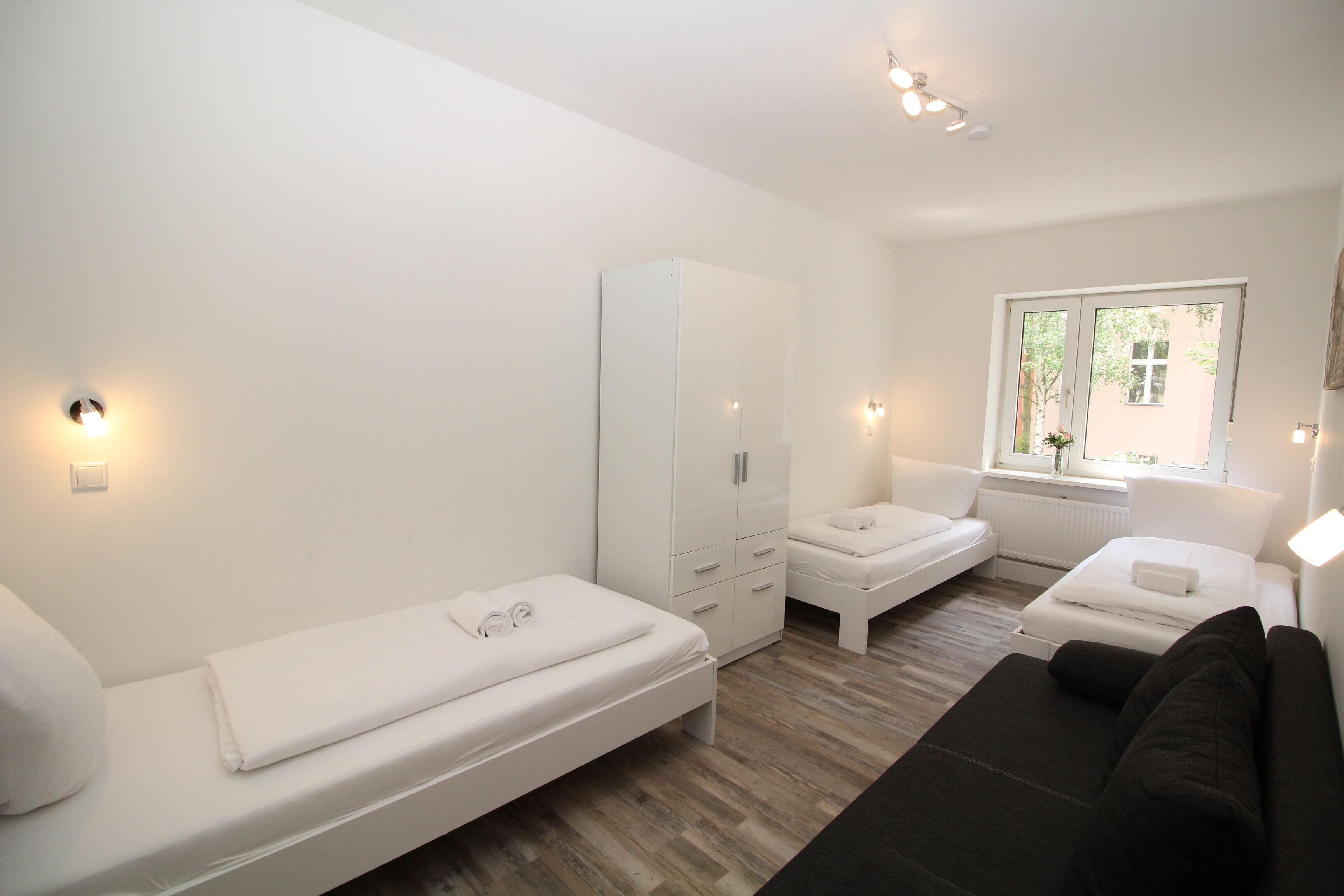 Een moderne hotelkamer met een eenpersoonsbed, een slaapbank, een kledingkast en een raam met uitzicht.