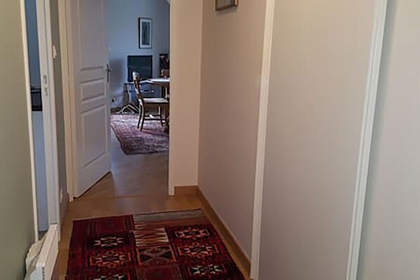 Un couloir étroit, orné d’un tapis à motifs, mène à un coin repas où se trouvent une table et des chaises.