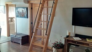 Een kamer met een houten ladder tegen een muur, een aan de muur bevestigde televisie, een houten bank en een plant op een tafel.