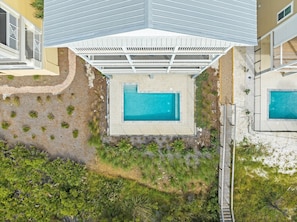 An aerial view of a property with two swimming pools, a covered patio area, and a landscaped garden.