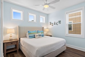 A bedroom with a bed, two nightstands, a ceiling fan, and a window with blinds.