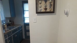 A small room with a grey sofa, a pillow with text, a framed tea set, and a kitchen in the background. - Nostalgic One-level Bungalow in perfect location! (Colorado Springs)