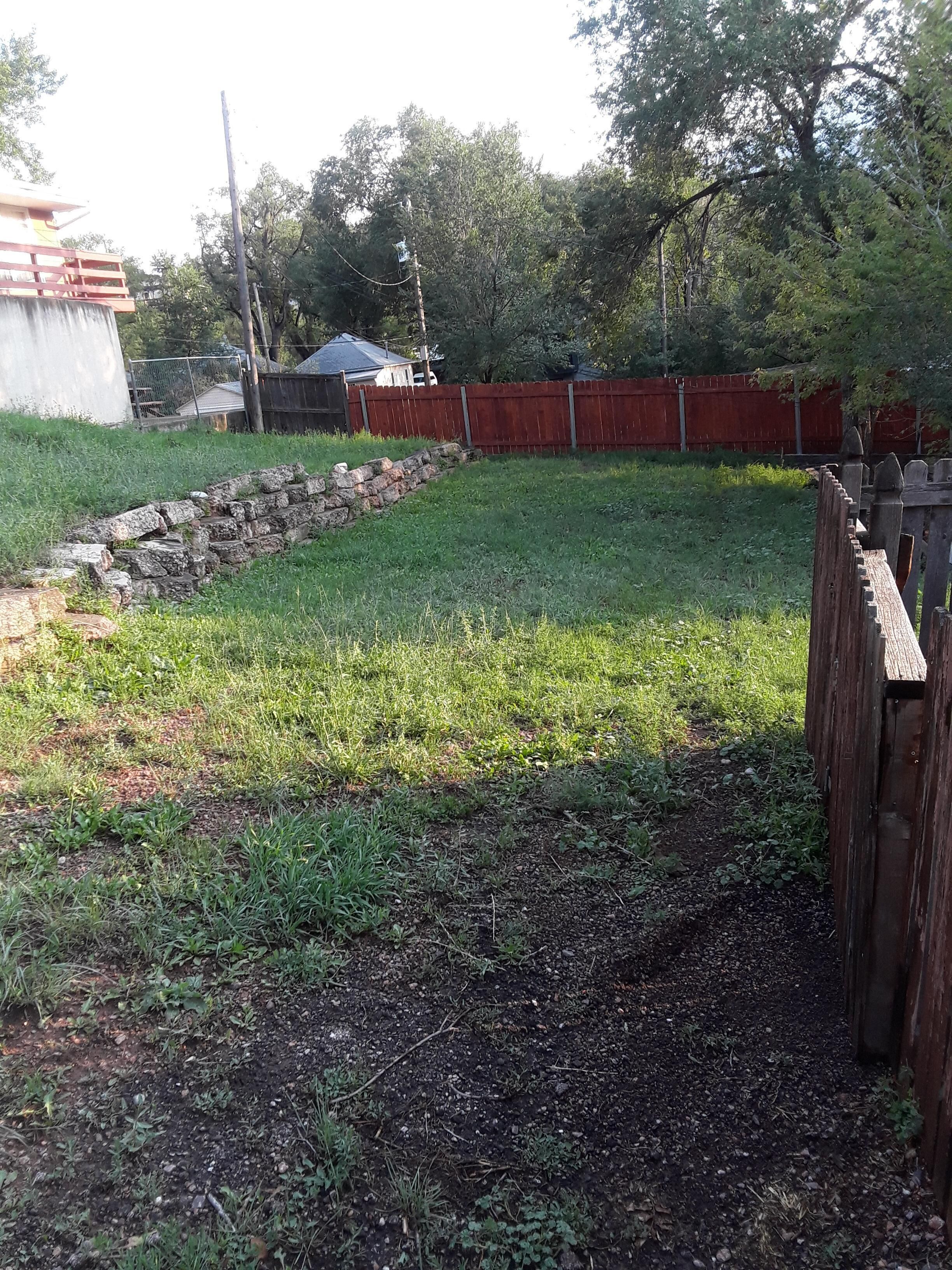 A backyard with a stone wall, a wooden fence, and a grassy area.