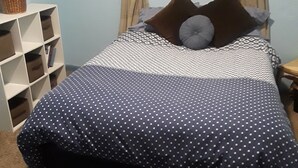 A neatly made bed with a polka dot cover, a bedside table, a window with curtains, and a bookshelf with a plant. - Nostalgic One-level Bungalow in perfect location! (Colorado Springs)