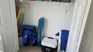 A storage area with shelves holding folded blankets, a blue table with bags, and a white cooler.