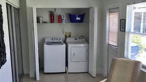 A laundry room with two washing machines, a fire extinguisher, and a blue laundry basket on a shelf.