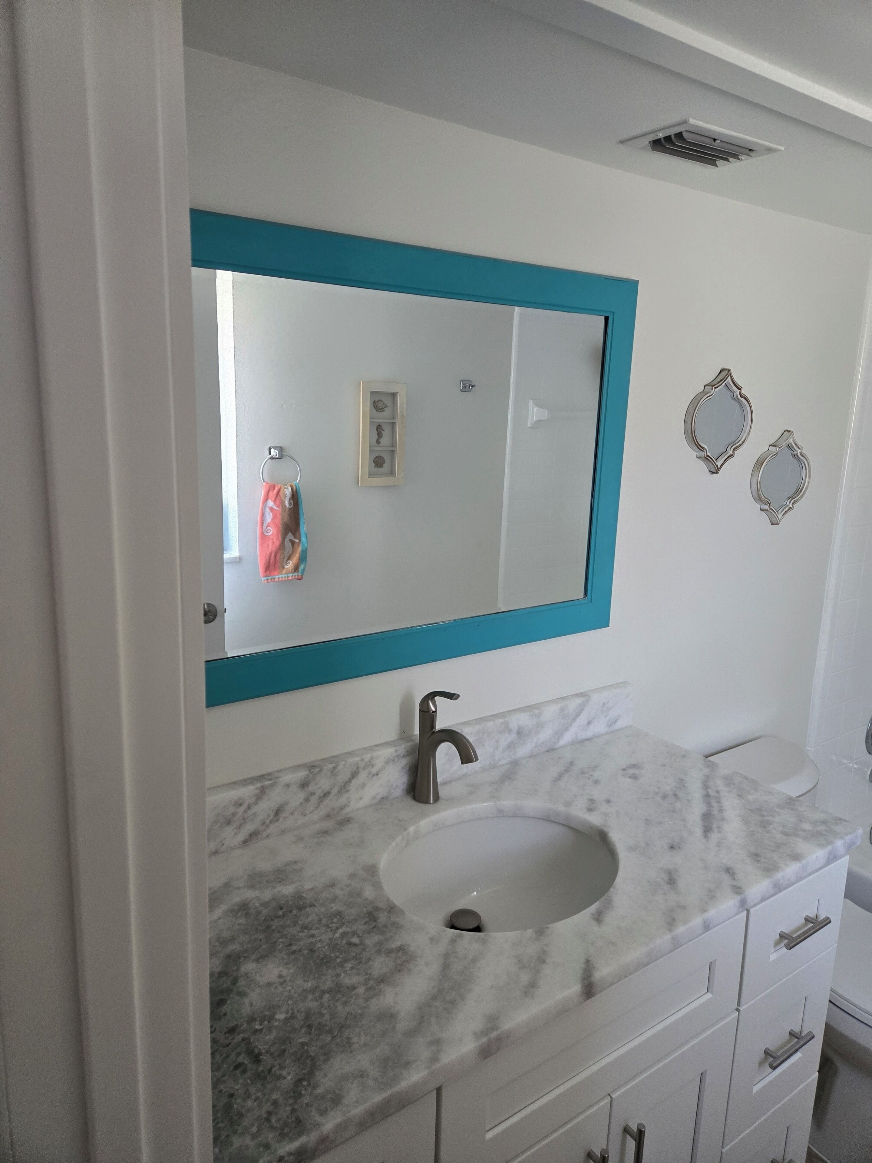 A bathroom with a white sink, a blue-framed mirror, and a marble countertop.