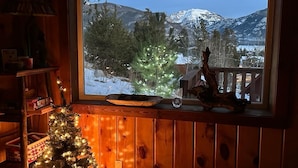 A cozy room with a wooden interior, a window with a view of snow-covered mountains, and a decorated Christmas tree.