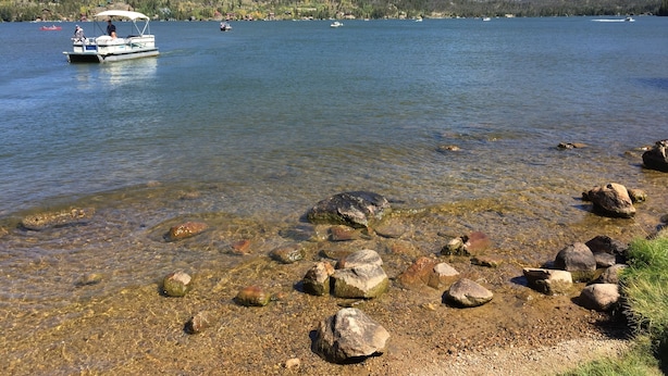 A lake with boats, clear water, and rocky shore.