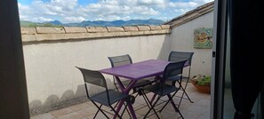 An outdoor patio with a purple table and four chairs, a potted plant, and a view of mountains in the background. - Medieval charm and soaring vistas in the heart of Provence: what's not to love? (Vaison-la-Romaine)