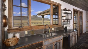 A kitchen with a large window, wooden cabinets, and a dishwasher. - Unique 40 AC Horse Friendly Ranch Renovated 1850 Miners Cabin w/3000 SF Addition (Gunnison)