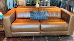 A brown leather sofa with a blue pillow, a vase with flowers, and a rustic kitchen with wooden cabinets and a dining area. - Unique 40 AC Horse Friendly Ranch Renovated 1850 Miners Cabin w/3000 SF Addition (Gunnison)
