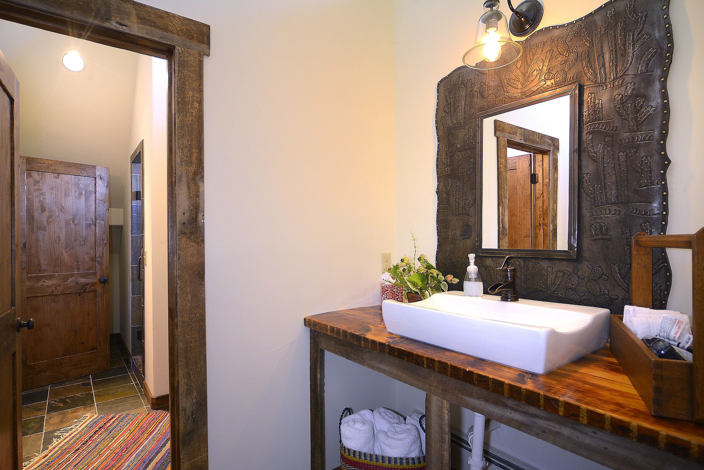 Un baño con tocador de madera, lavabo blanco, espejo con marco decorativo y perchero.